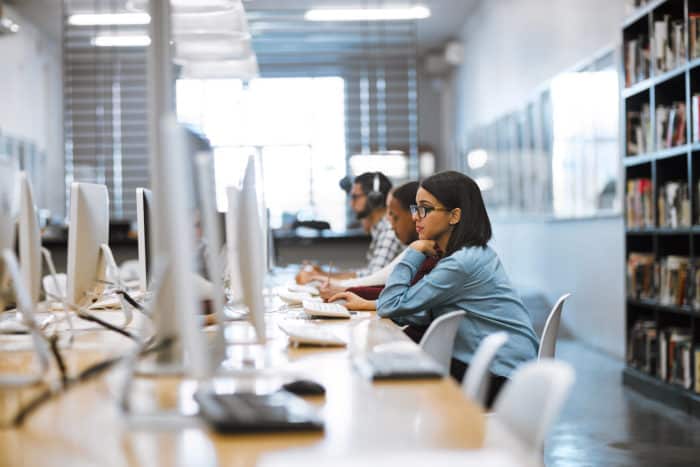 Captură cu un grup de studenți care lucrează la computere în biblioteca din campus