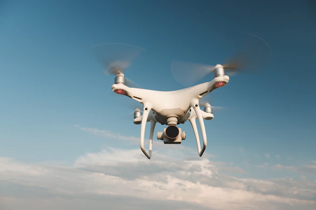 Drone branco de foto grátis pairando em um céu azul brilhante