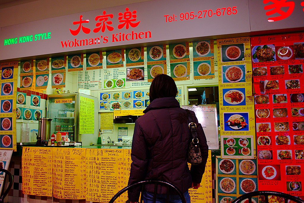 Fotografía de la parte trasera de un cliente frente a un restaurante de Hong Kong con abrumadoras opciones de menú que requieren docenas de imágenes, carteles y letreros para explicar