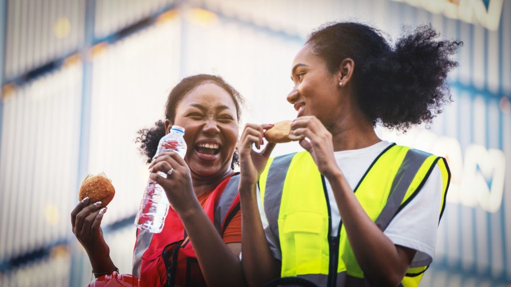 Zwei Arbeiterinnen lachen und essen in der Pause