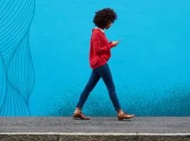 امرأة من الجيل Z تمشي على الرصيف أمام جدار أزرق لامع ذو نسيج عضوي. تمثل المرأة والملمس العلاقة بين احتياجات المشتري وتوقعاته وقدرة البائع على النجاح من خلال تكريم العميل.