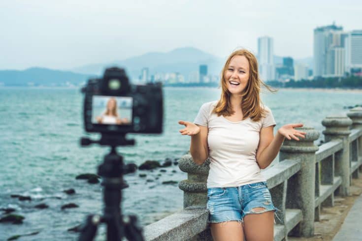 Una mujer filmando un vlog frente a un muelle.