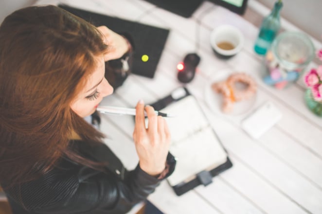 mulher se senta e pensa em uma mesa com lanches, uma caneca de café e um caderno aberto