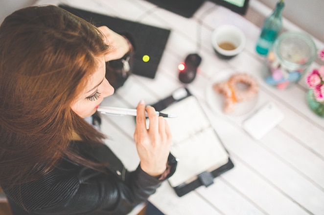 une femme mâche un stylo en pensant à son bureau