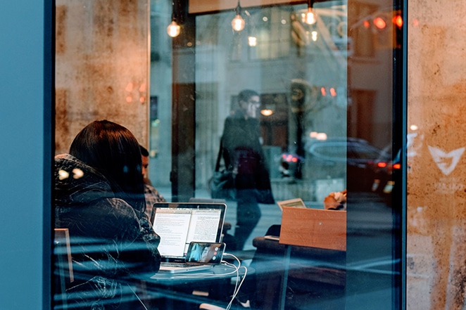 Une femme travaille dans un café ; un homme parlant au téléphone peut être vu à travers les fenêtres