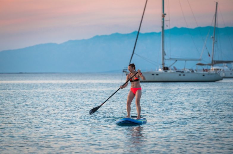 Imagen de stock de una mujer haciendo paddle surf en las aguas azules del lago Glacier frente a un cielo Gossamer Pink